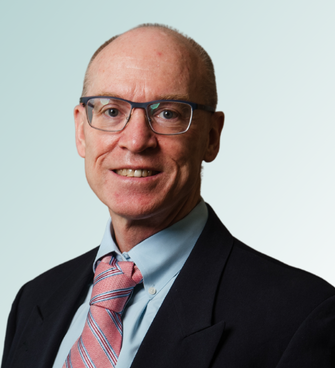 A middle-aged man with thinning hair and glasses is smiling. He is wearing a dark blazer, light blue shirt, and pink striped tie. The background features a light gradient. Dr. Curtis Leonard, MD exudes professionalism and warmth in his attire and demeanor.