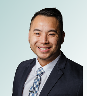 A person with short, dark hair and a neatly trimmed beard, Dr. Jeffrey Ebel, is smiling at the camera. They are wearing a dark blazer over a white shirt and a blue and white checkered tie. The background is a plain, light gradient.