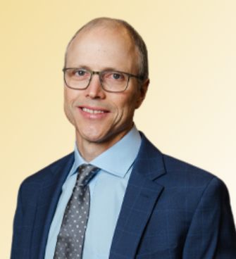 man smiling, wearing glasses and a suit and tie