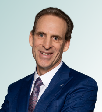 Matthew A. Javernick, MD, a man with short, brown hair, is smiling at the camera. He is wearing a dark blue suit, a white dress shirt, and a patterned tie. The background is a light blue gradient.