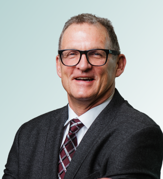 A man with short, grayish hair and glasses is smiling while facing the camera. Identified as Peter Wood, MD, he is wearing a dark gray suit, a white shirt, and a red and white patterned tie. The background is a light gradient blue.