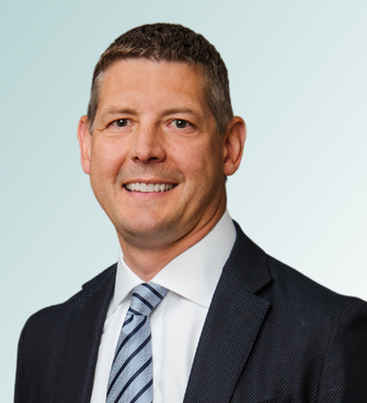 A professional man with short, dark hair is smiling. Robert FitzGibbons, MD, is wearing a dark suit jacket, a white dress shirt, and a striped tie against a pastel blue background.