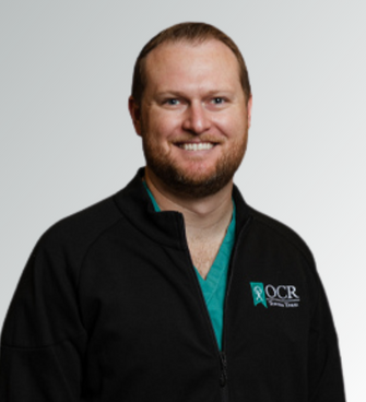 man smiling, wearing a black jacket and a medical scrubs