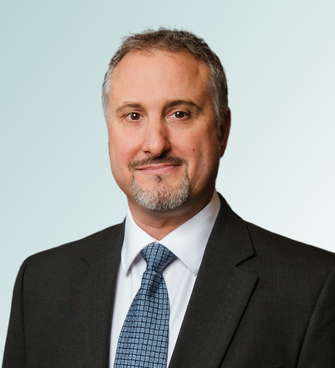 A man with short gray hair, light facial hair, and a friendly expression is wearing a dark suit, white shirt, and patterned blue tie. MD Robert FitzGibbons stands against a light gradient background.