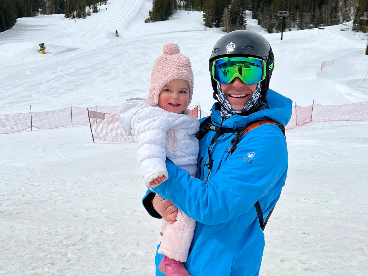 a man in a blue jacket in the snow holding a baby 