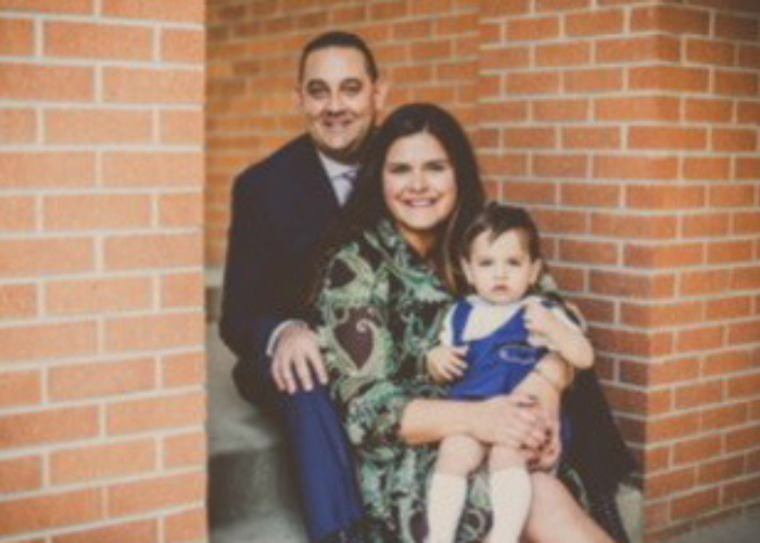 a family of three posing in front of a brick wall