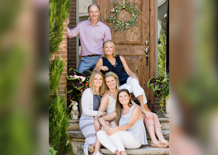 A family of 5 sitting on the steps in front of a door