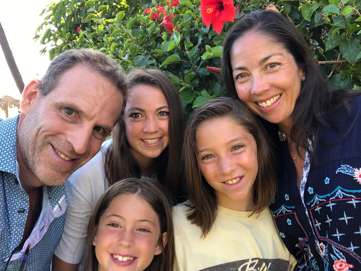 A family of 5 smiling in front of some flowers