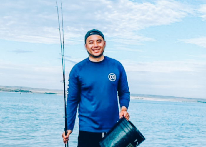 A man holding a fishing pole and bucket in a blue shirt