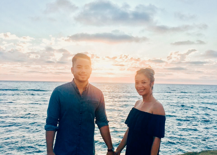 A man and woman holding hands in front of a sunset over the ocean