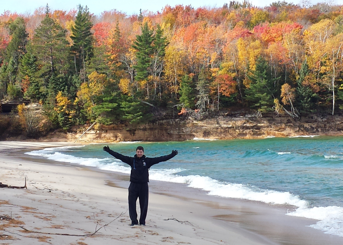 a man standing with his arms open in front of a lake and colorful trees