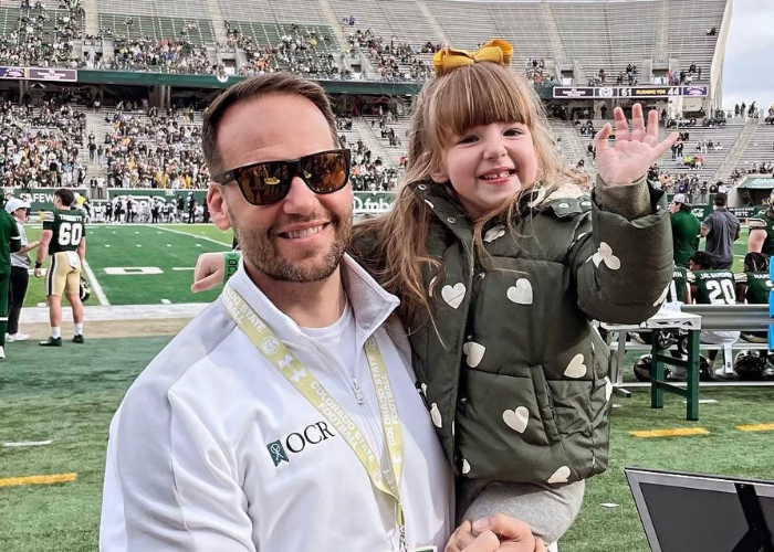 a man holding a kid on the sidelines of a football field