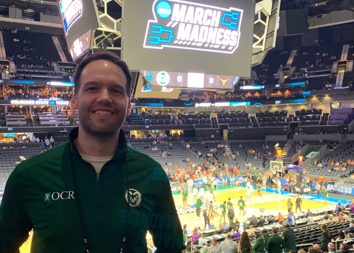 Dr. Lancaster standing in front of a March Madness basketball court