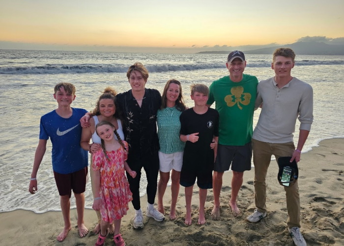 a family of 7 standing on a beach in front of the ocean at sunset