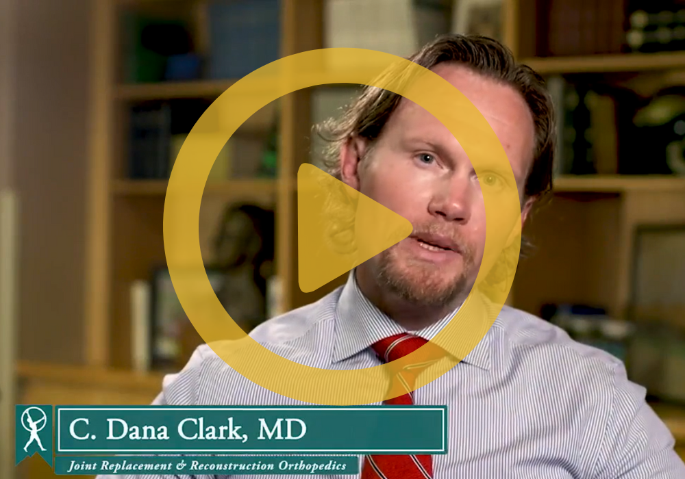 Dr. Clark standing in front of a book case with a play button on the forefront