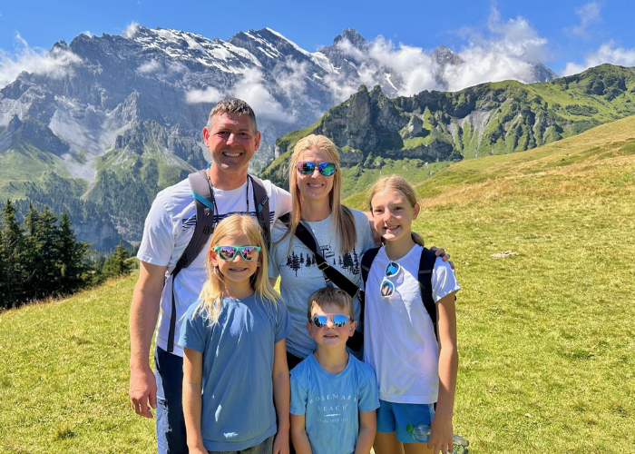 A family of 5 with back packs on standing in front of a mountain on a hike