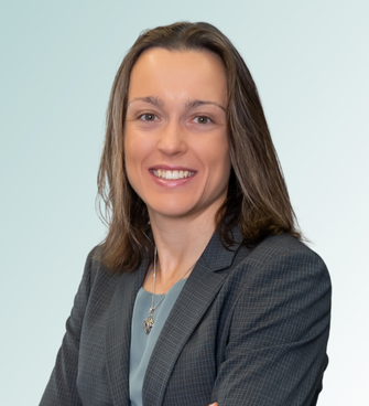 Cara Thorne, MD, with shoulder-length brown hair, is smiling and looking at the camera. She is wearing a grey blazer over a light blue blouse, with a necklace visible. The background is a gradient of light blue to white.