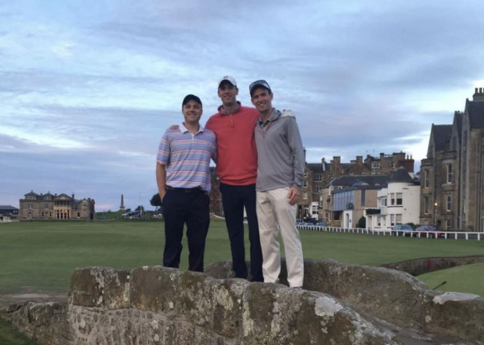 Dr. Johnson stands on a bridge on a golf course with two of his friends on an overcast day.